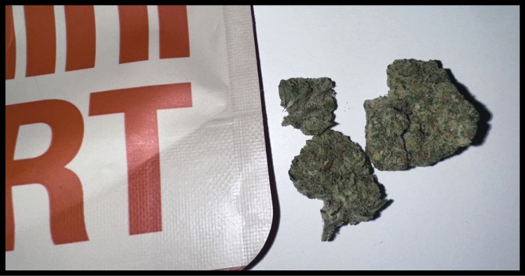 A close-up, high-contrast shot of Mini MART cannabis packaging on a dark slate surface with the text "EXQUISITE sativa" visible in the background.