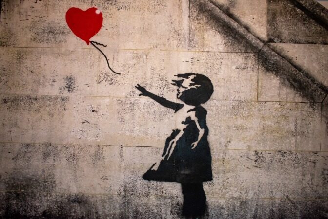 Stencil of a young girl releasing a heart-shaped balloon on a wall