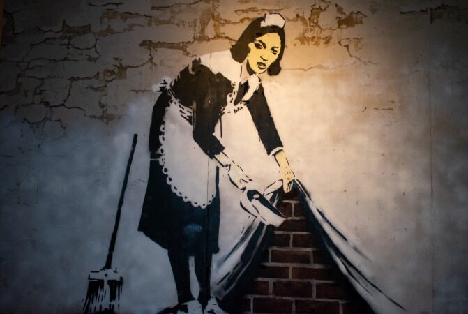Banksy mural of a maid lifting a wall to reveal bricks underneath