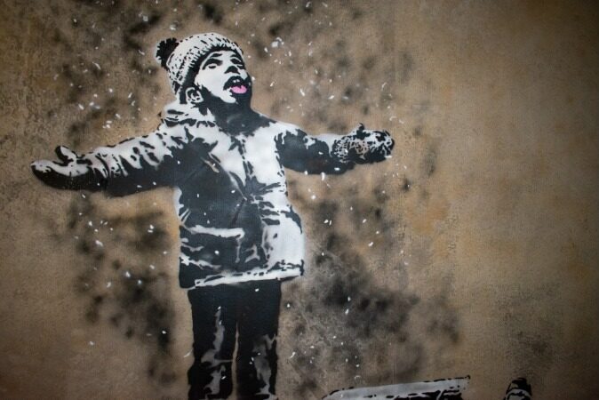 Banksy-style stencil of a child standing in falling snow with arms open