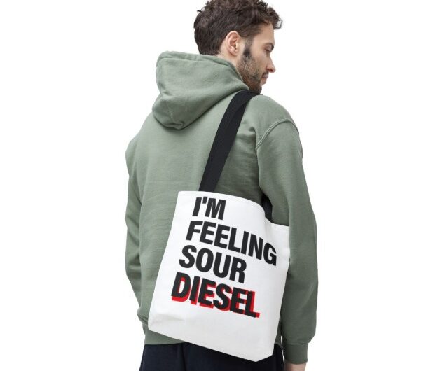 Man wearing green hoodie carrying white tote bag with "I'm Feeling Sour Diesel" design.